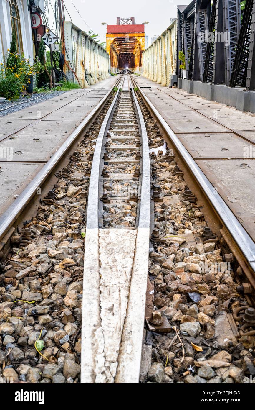 Nel quartiere vecchio della città nel Vietnam del Nord, un unico binario ferroviario conduce attraverso il vecchio ponte in acciaio coloniale francese, che attraversa la R di Hanoi Foto Stock