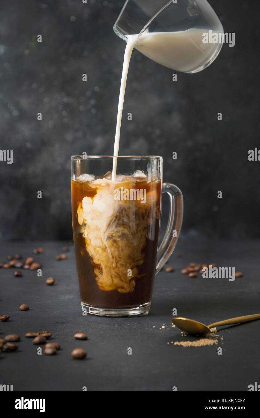 Caffè a latte freddo in bicchiere da tazza con latte versato sul nero Foto Stock
