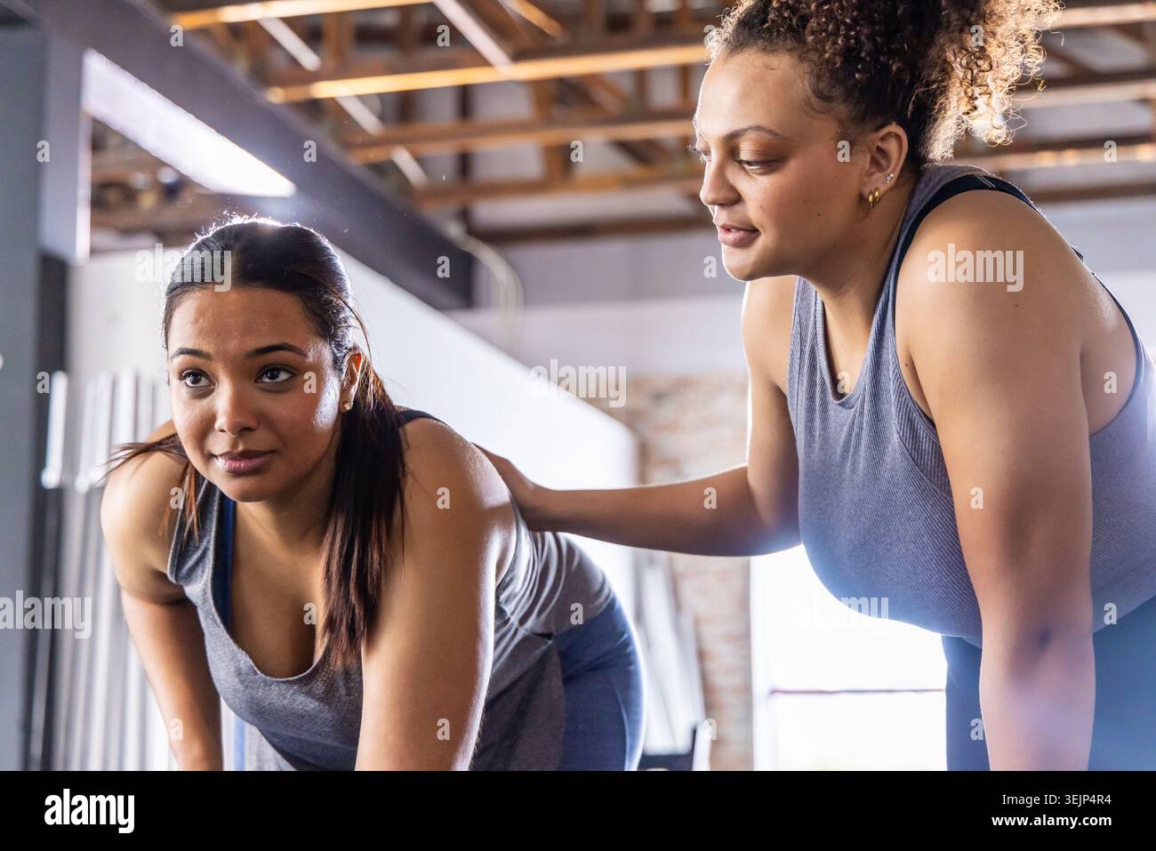 Diverse formatrici di abbigliamento atletico guidano il cliente a muoversi piegato in palestra con travi. Fitness, movimento, coaching, stallone Foto Stock