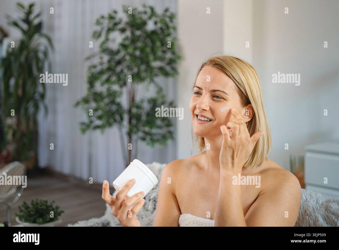 Giovane donna che applica crema viso a casa Foto Stock