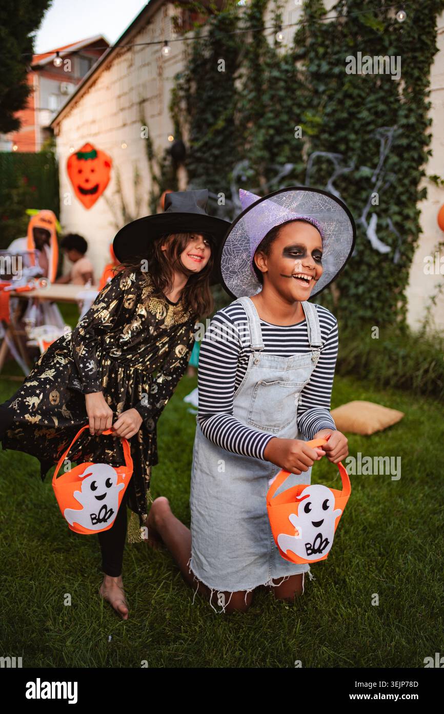 Due allegre ragazze che indossano costumi di Halloween che tengono i secchi in giardino Foto Stock