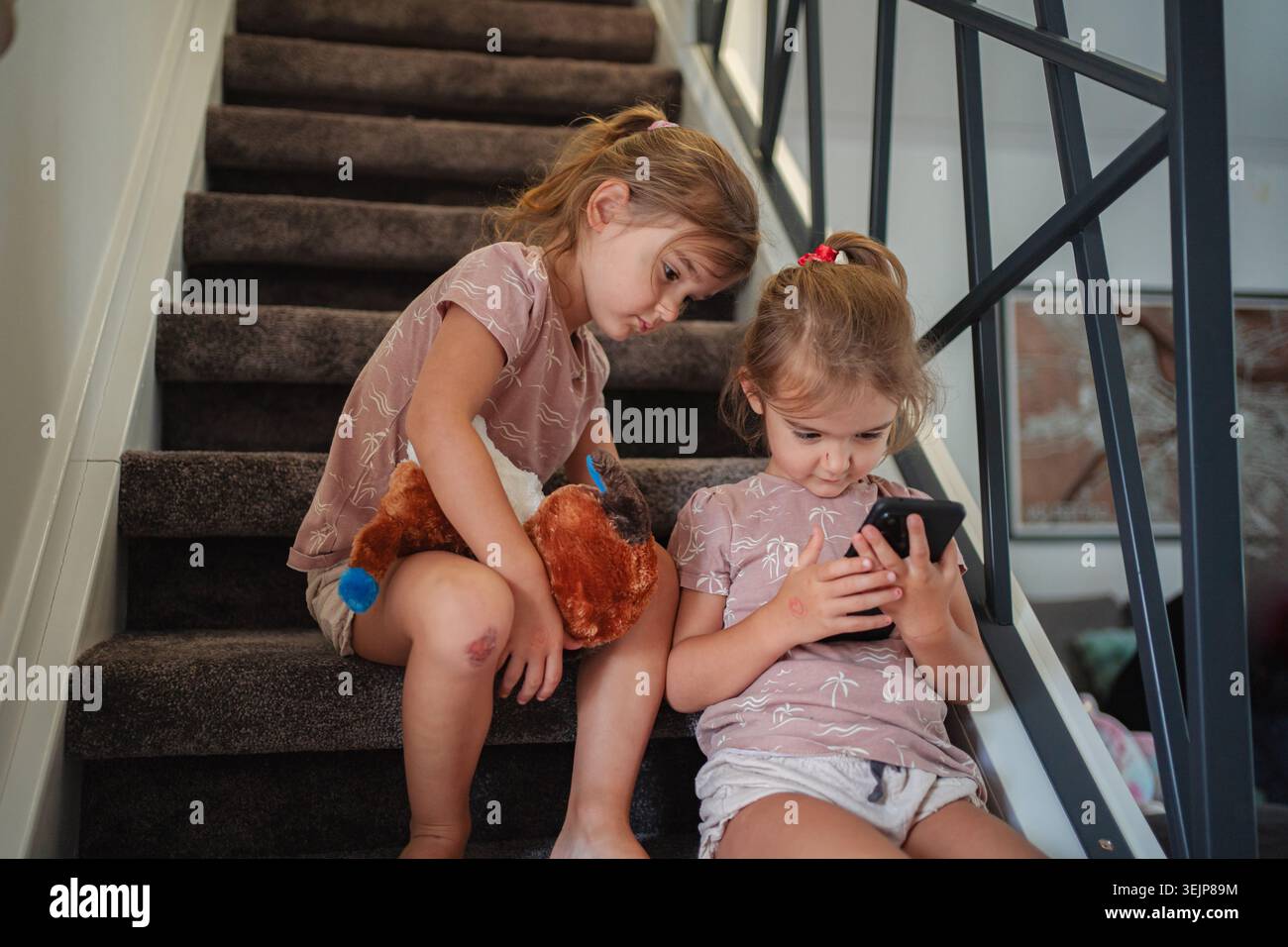 Due ragazze in età prescolare che giocano con lo smartphone sulle scale di casa Foto Stock