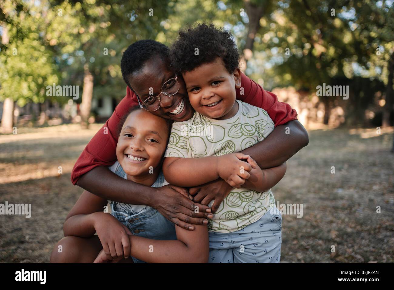 Madre che abbraccia i suoi due figli in un parco Foto Stock