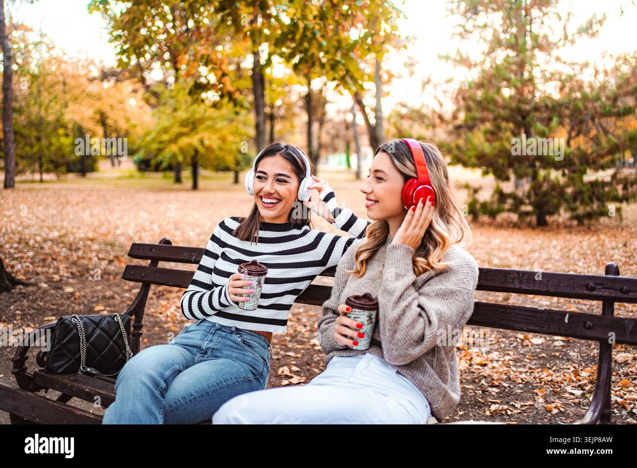 Due ragazze si godono le vibrazioni autunnali mentre sorseggiano un caffè nel parco Foto Stock