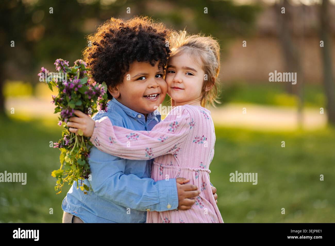 Due bambini diversi che si abbracciano nel parco con fiori selvatici freschi Foto Stock