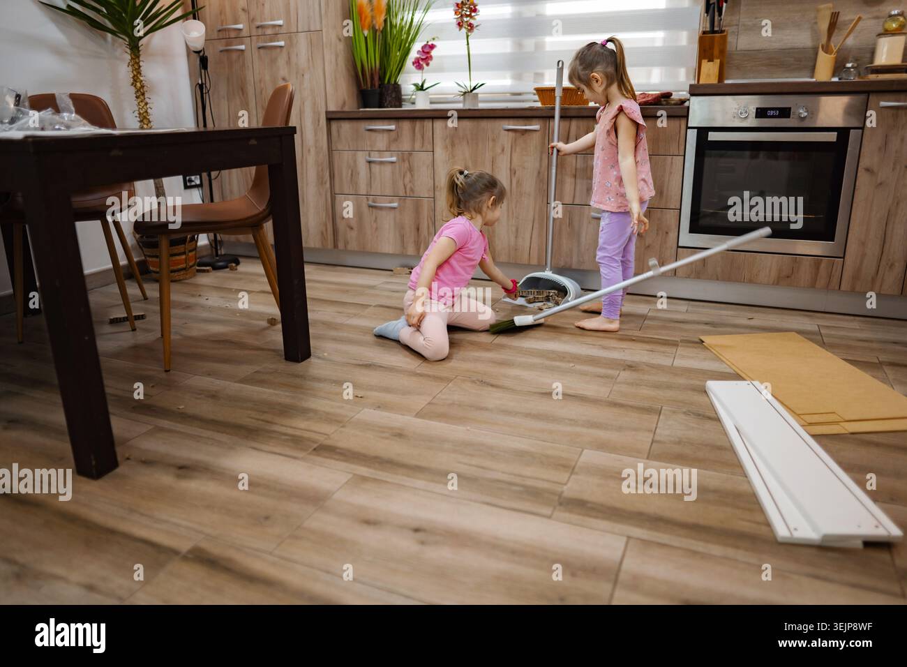 Due bambini puliscono con gioia la cucina in un pomeriggio di sole Foto Stock