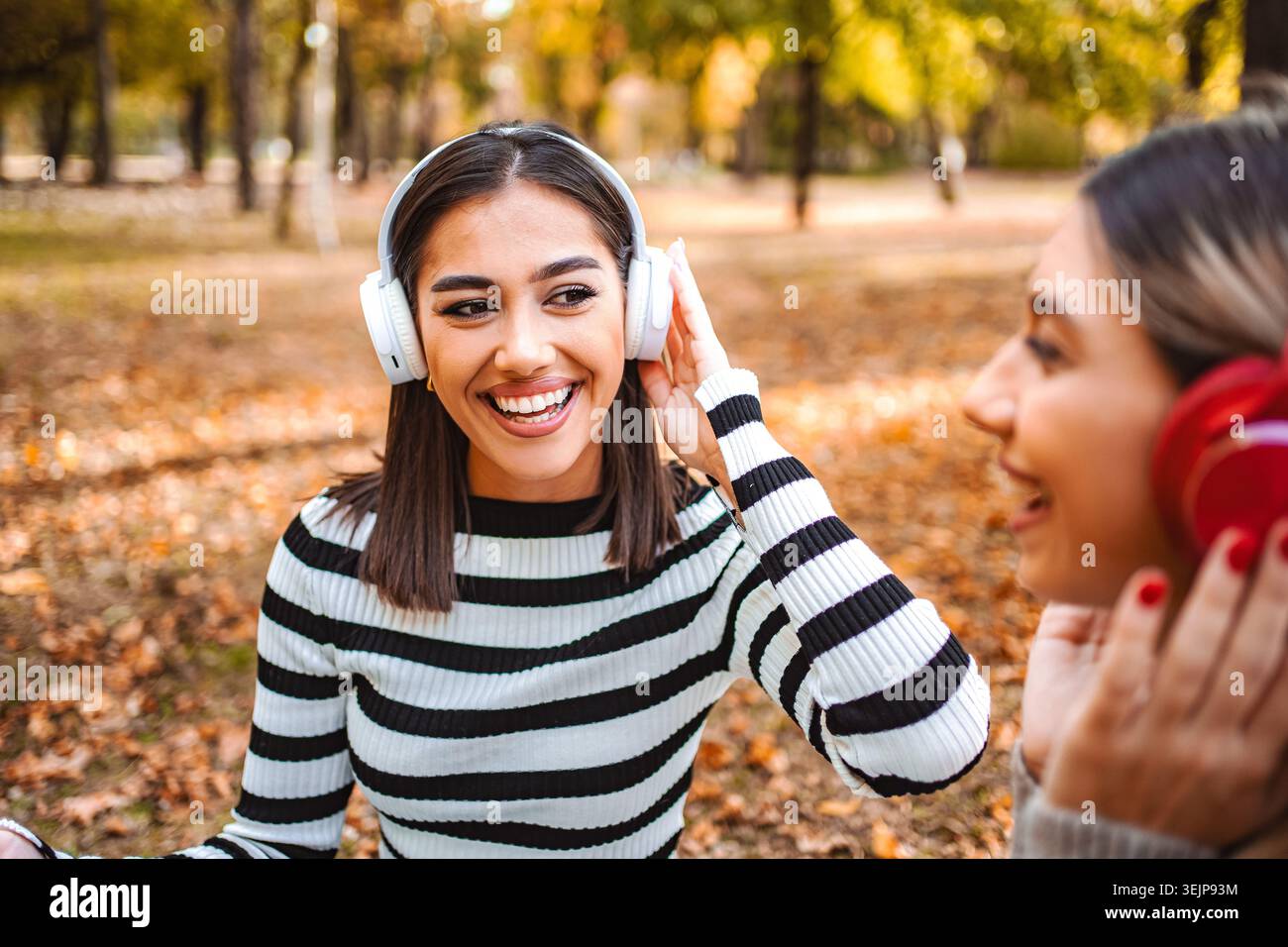Allegri momenti autunnali mentre due ragazze condividono la musica in un parco vivace Foto Stock