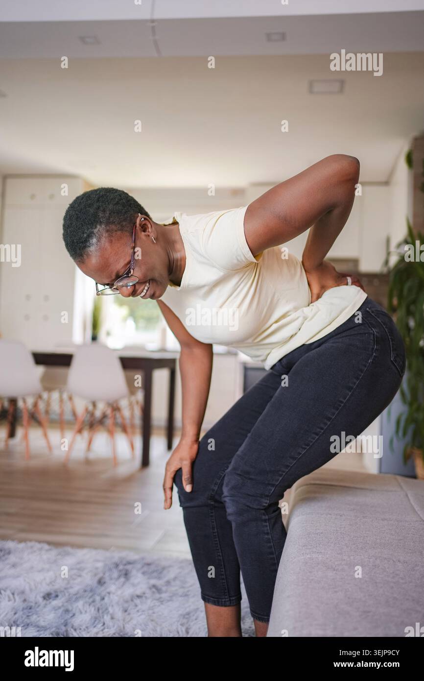 Giovane donna che soffre di mal di schiena e ginocchio a casa Foto Stock