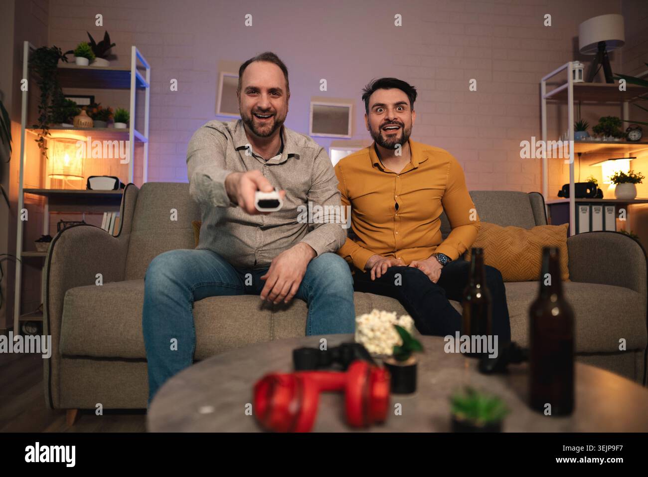 L'emozione riempie il salotto mentre due amici si divertono con una serata di gioco emozionante con risate e spuntini fino a tarda sera Foto Stock