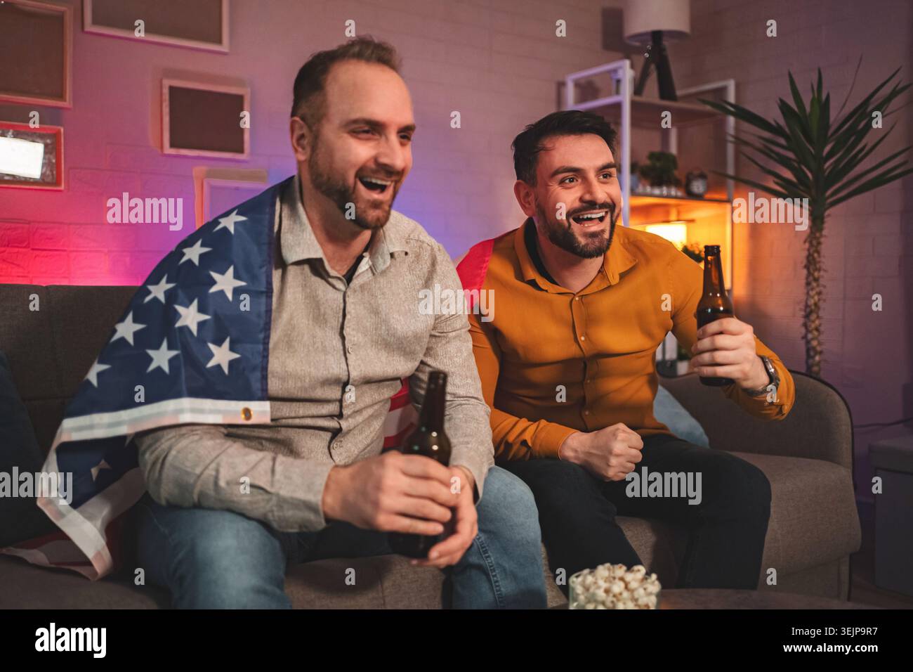 Amici che si godono la serata di gioco a casa con spuntini e bevande sotto l'illuminazione calda Foto Stock
