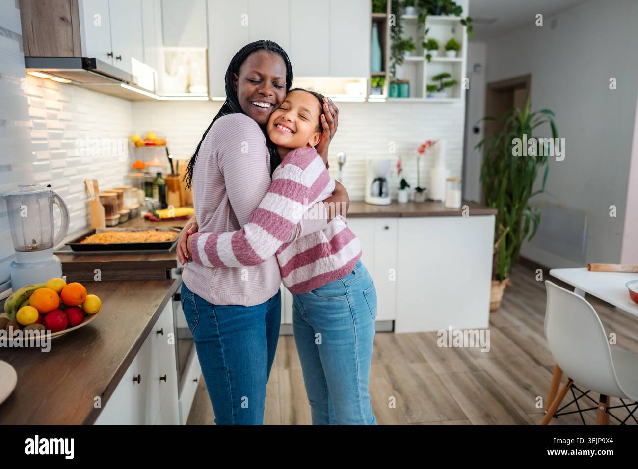 Madre e figlia abbracciano con amore nella cucina moderna Foto Stock