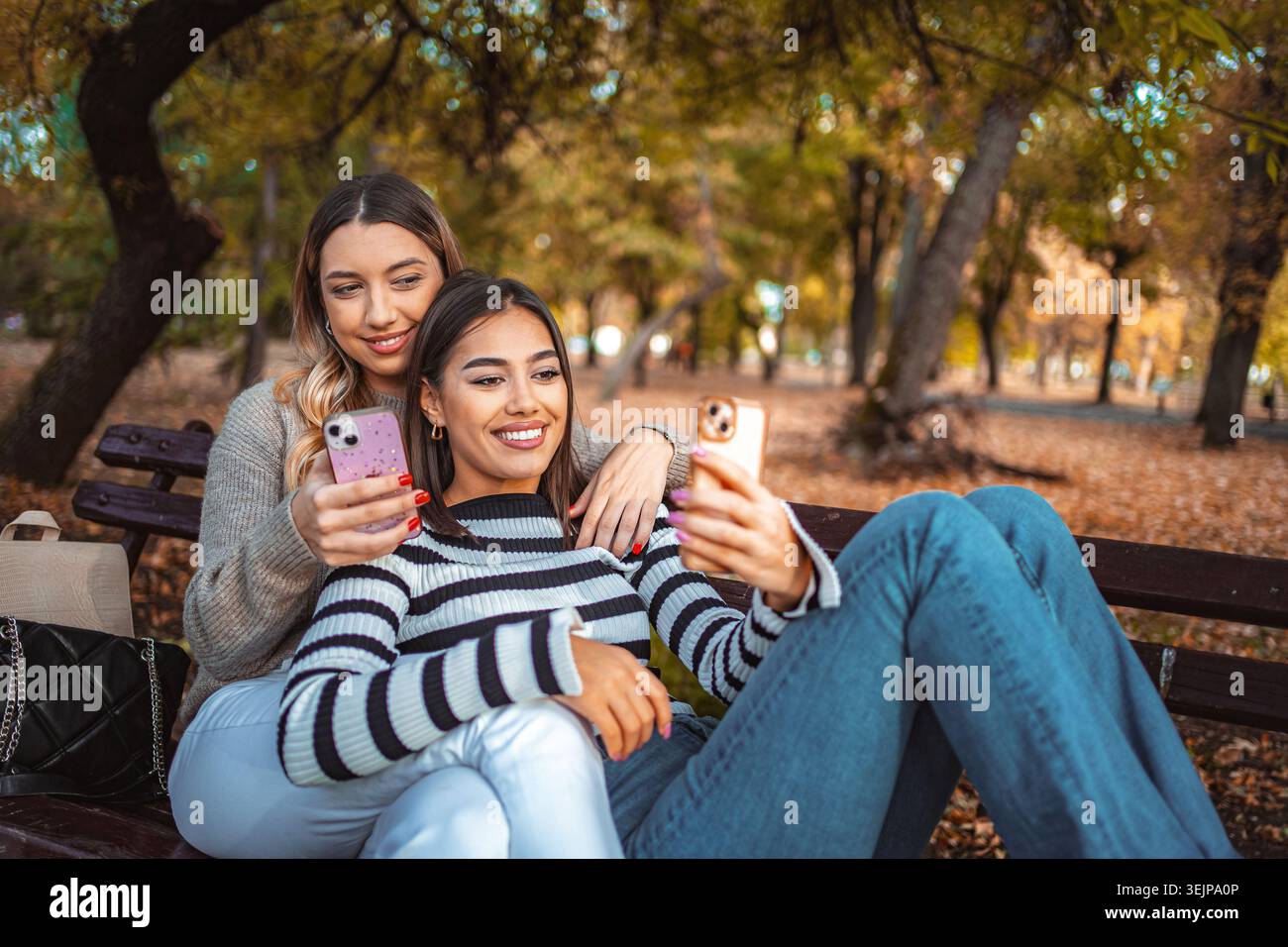 Due ragazze condividono un momento di gioia in un parco autunnale mentre scattano selfie Foto Stock