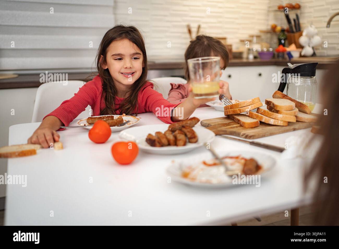 Ragazze felici che fanno colazione in cucina con succo di frutta e salsiccia Foto Stock