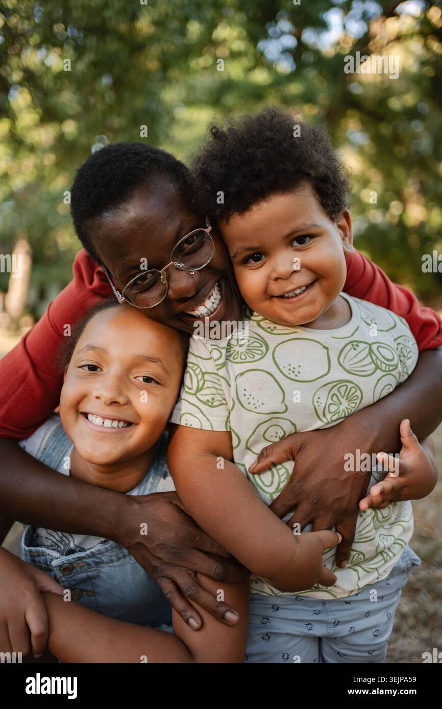 Madre che abbraccia i suoi due figli in un parco Foto Stock