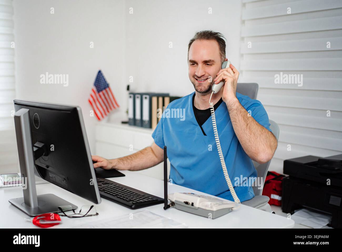 Infermiera maschile che parla al telefono e usa il computer Foto Stock