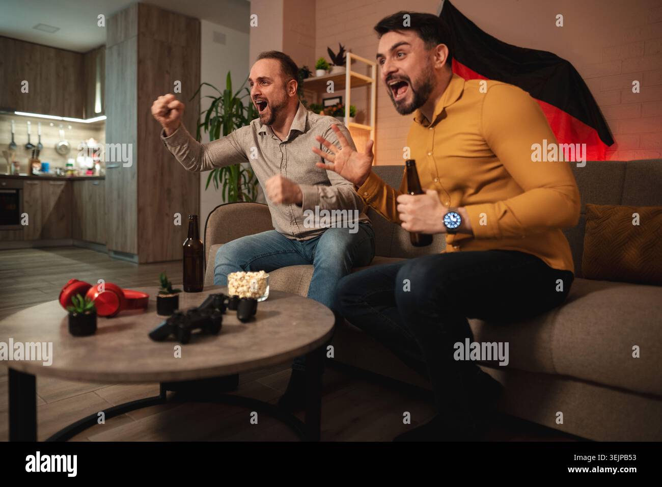 Amici che festeggiano insieme mentre guardano un'emozionante partita sportiva nel loro accogliente salotto durante una serata emozionante Foto Stock