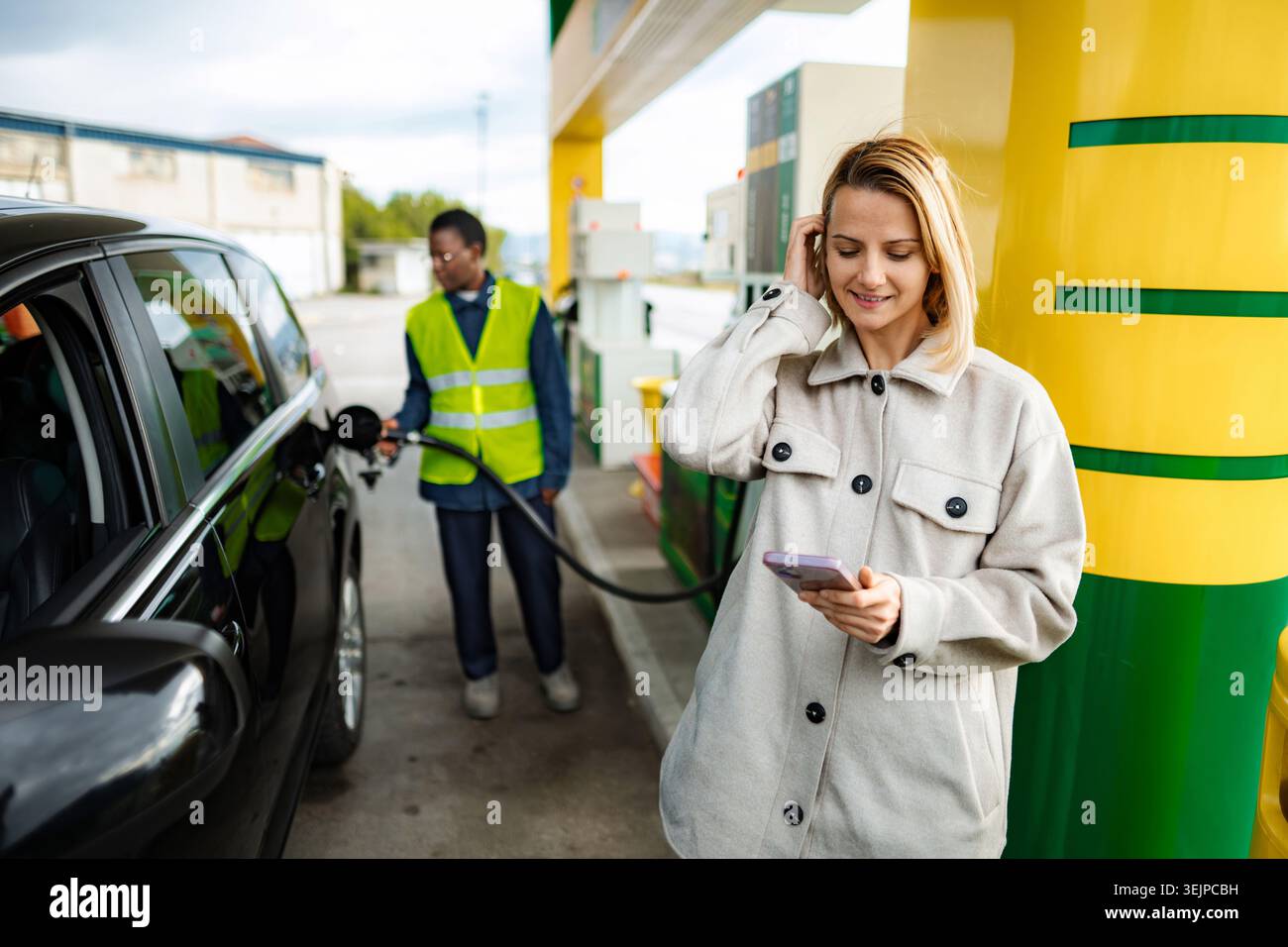 Donna che usa lo smartphone mentre fa rifornimento di carburante all'auto Foto Stock