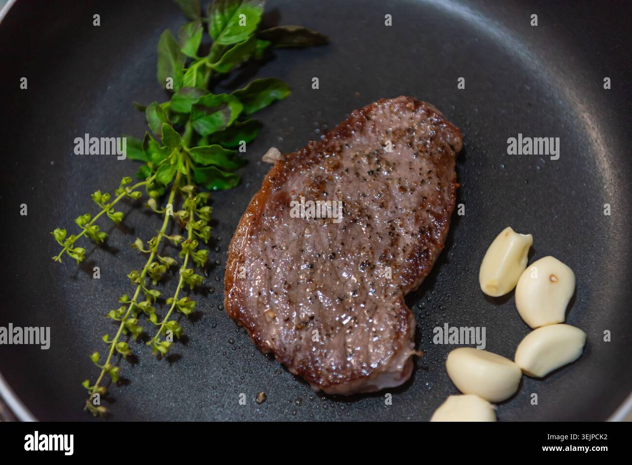 Succosa bistecca scottata in padella, cucinata con aglio fresco e basilico in una padella che mette in risalto la cucina gourmet, il sapore ricco e l'eccellenza della cucina casalinga Foto Stock