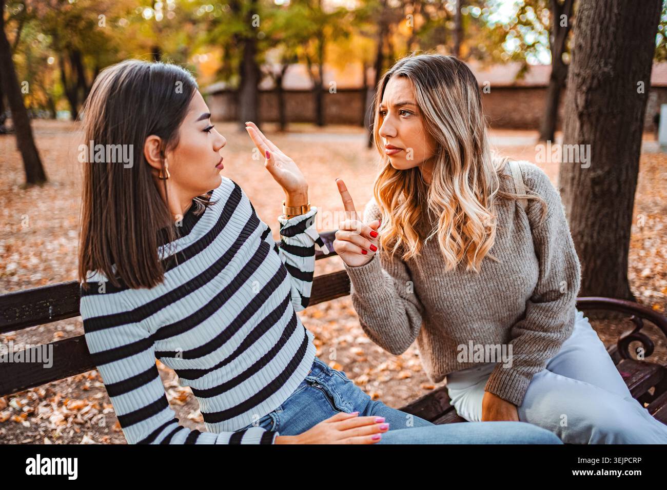 Due ragazze che condividono un momento emotivo su una panchina in uno scenario autunnale Foto Stock