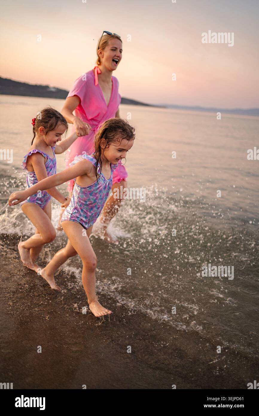Famiglia felice con madre e due figlie che spruzzano in mare al tramonto Foto Stock