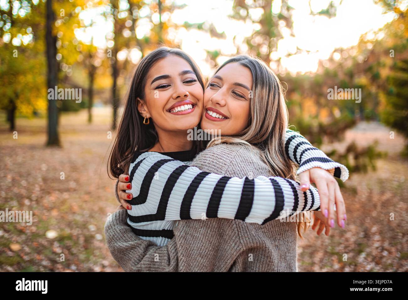 Due ragazze condividono un gioioso abbraccio in un parco autunnale pieno di foglie colorate Foto Stock