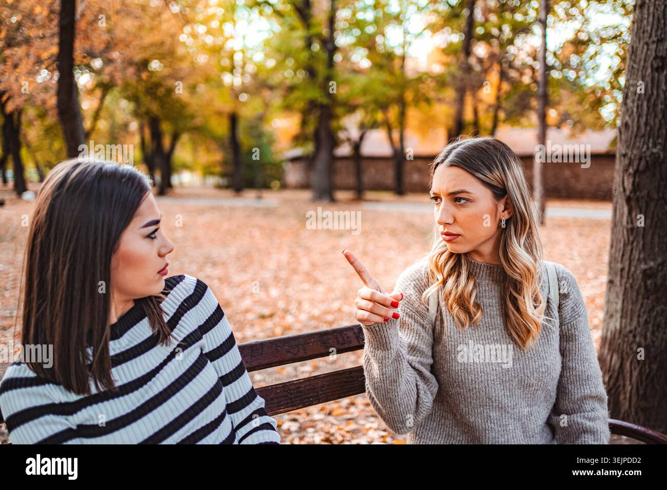 Due ragazze condividono una conversazione sentita in un colorato parco autunnale Foto Stock