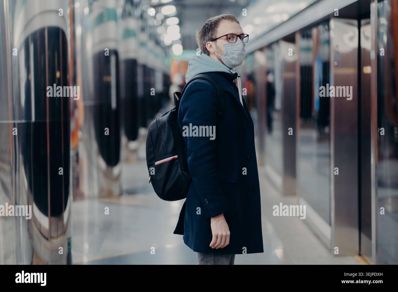 Misure preventive nei luoghi pubblici. Lateralmente girato di uomo in piedi maschera medica sulla stazione della metropolitana, porta zaino, sembra worr Foto Stock