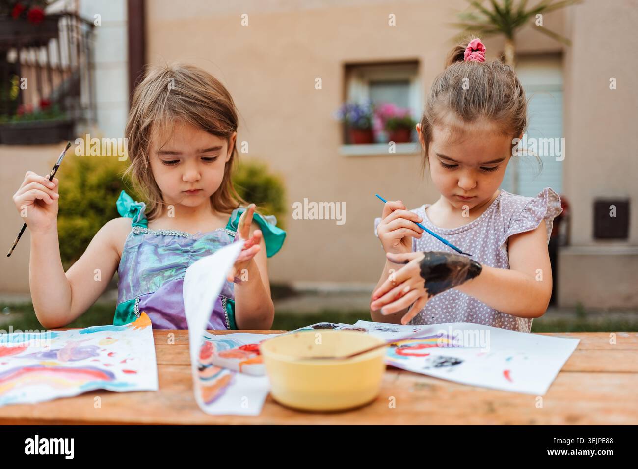 Due ragazze in età prescolare che dipingono con acquerelli su un tavolo di legno nel cortile posteriore Foto Stock