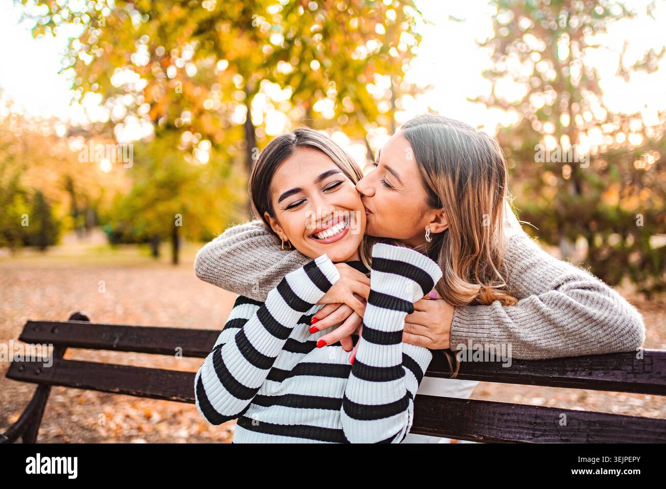 Due ragazze condividono risate e gioia in un parco autunnale pieno di foglie colorate Foto Stock