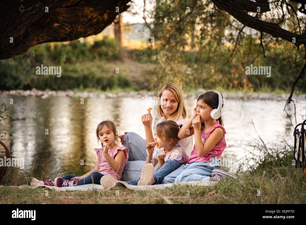 Madre che fa un picnic con le sue tre figlie vicino al fiume Foto Stock