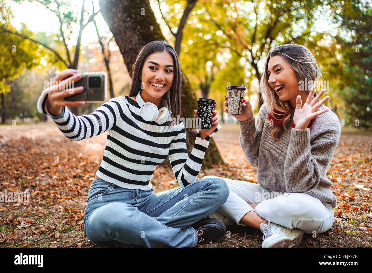 Due amici catturano la gioia autunnale con caffè e risate nel parco Foto Stock