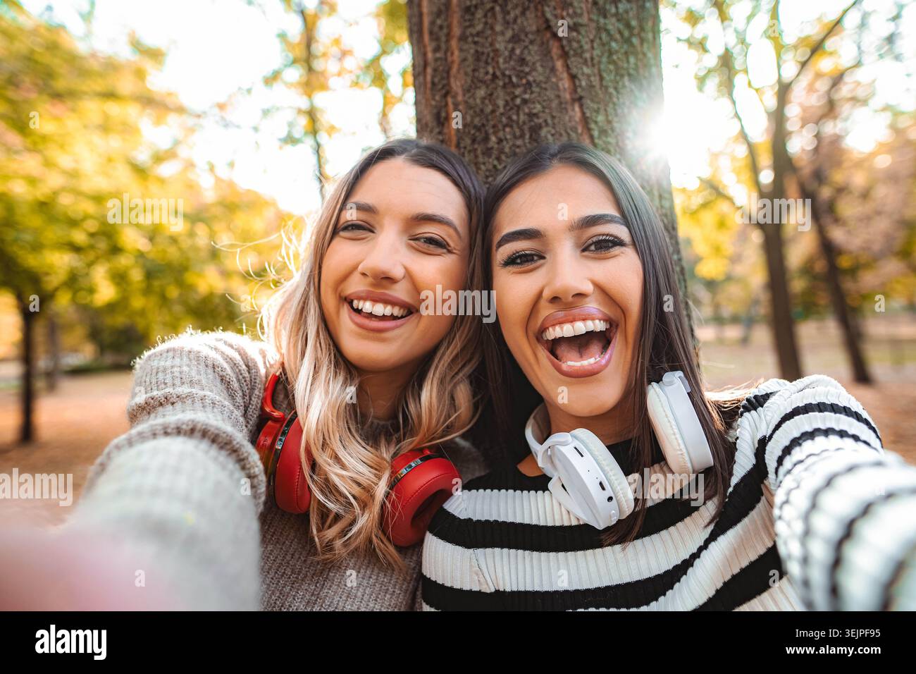 Due ragazze che si godono i sorrisi autunnali e l'amicizia in un parco illuminato dal sole Foto Stock