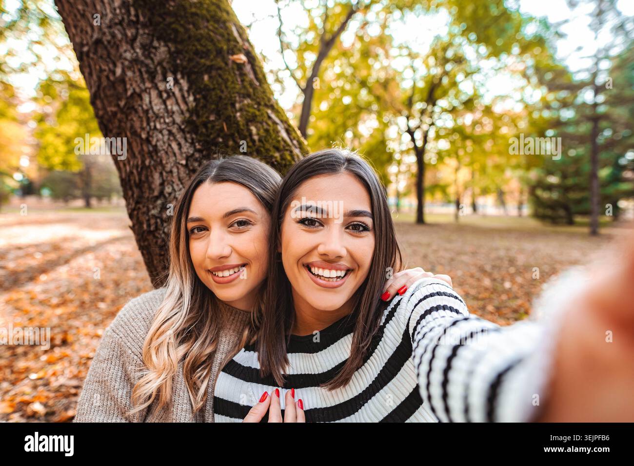 Due ragazze condividono un momento di gioia in un colorato parco autunnale pieno d'amore Foto Stock