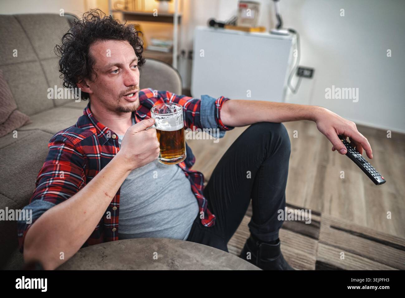 Uomo rilassato che beve birra e guarda la tv a casa Foto Stock