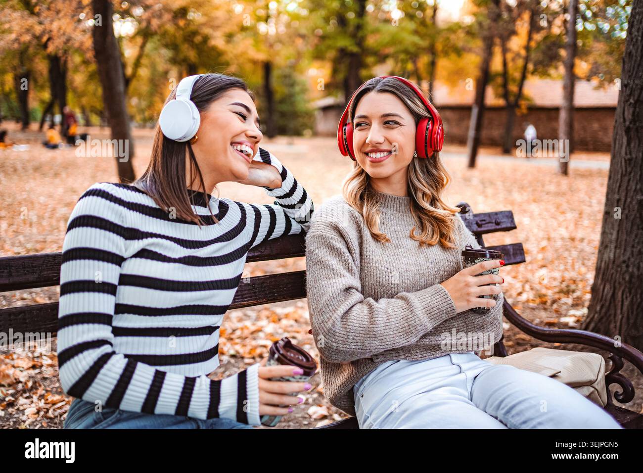 Due ragazze si godono le foglie d'autunno mentre condividono musica e risate nel parco Foto Stock