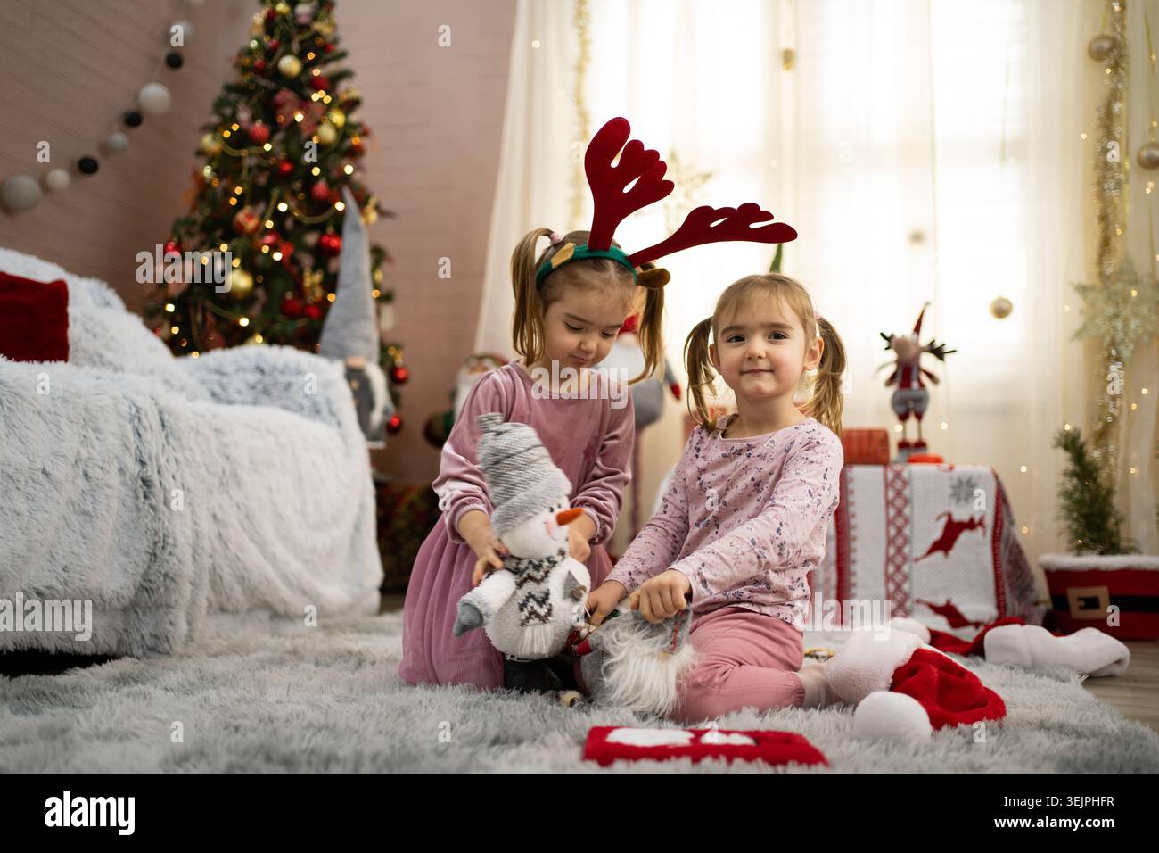 Due sorelle stanno giocando con le decorazioni natalizie vicino all'albero di natale Foto Stock