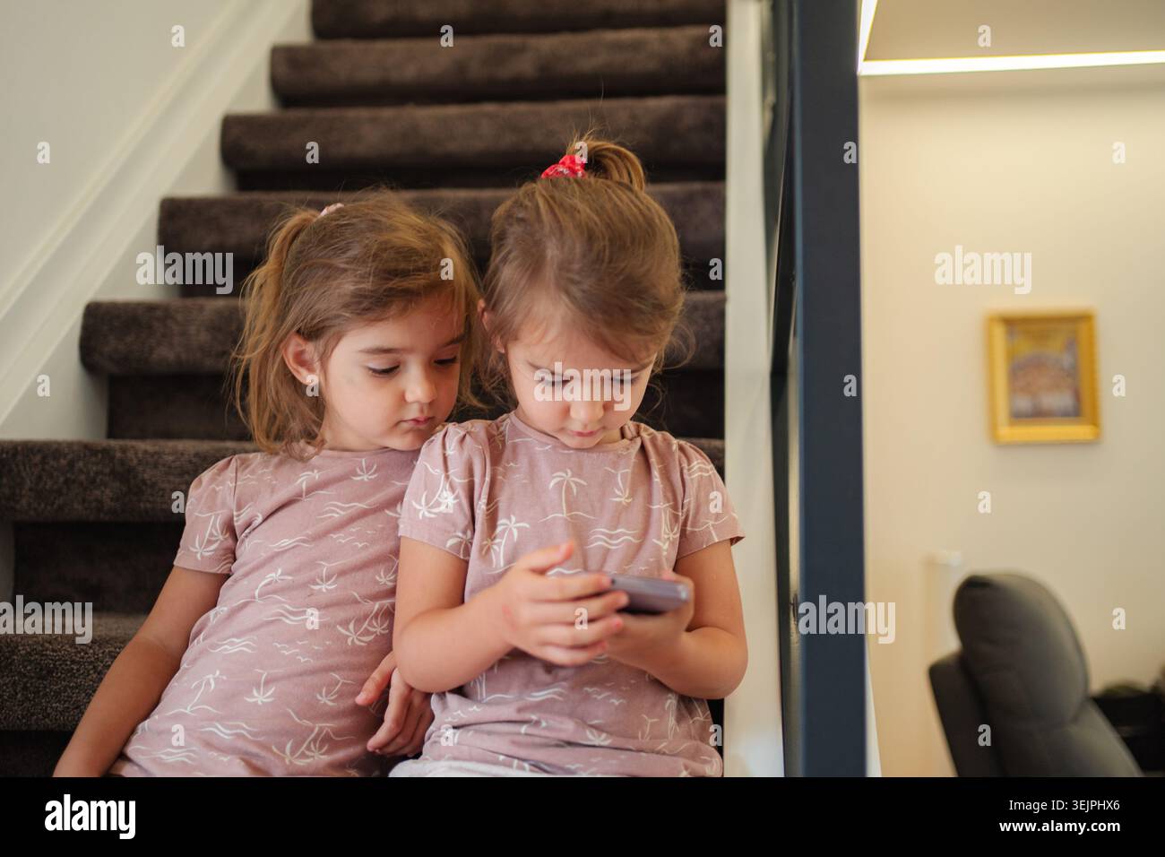 Due ragazze in età prescolare che giocano con uno smartphone sulle scale di casa Foto Stock
