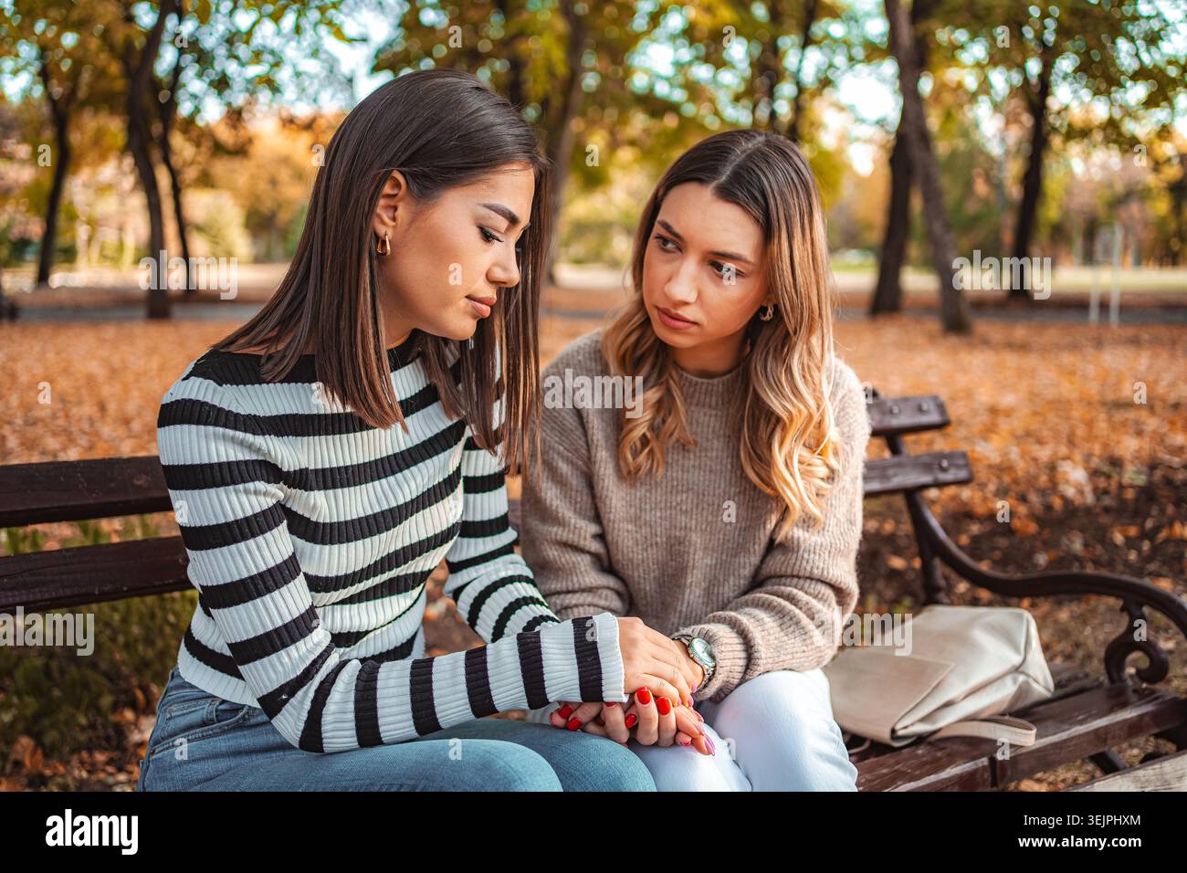 Due ragazze siedono vicino su una panchina del parco circondata da vivaci foglie autunnali Foto Stock