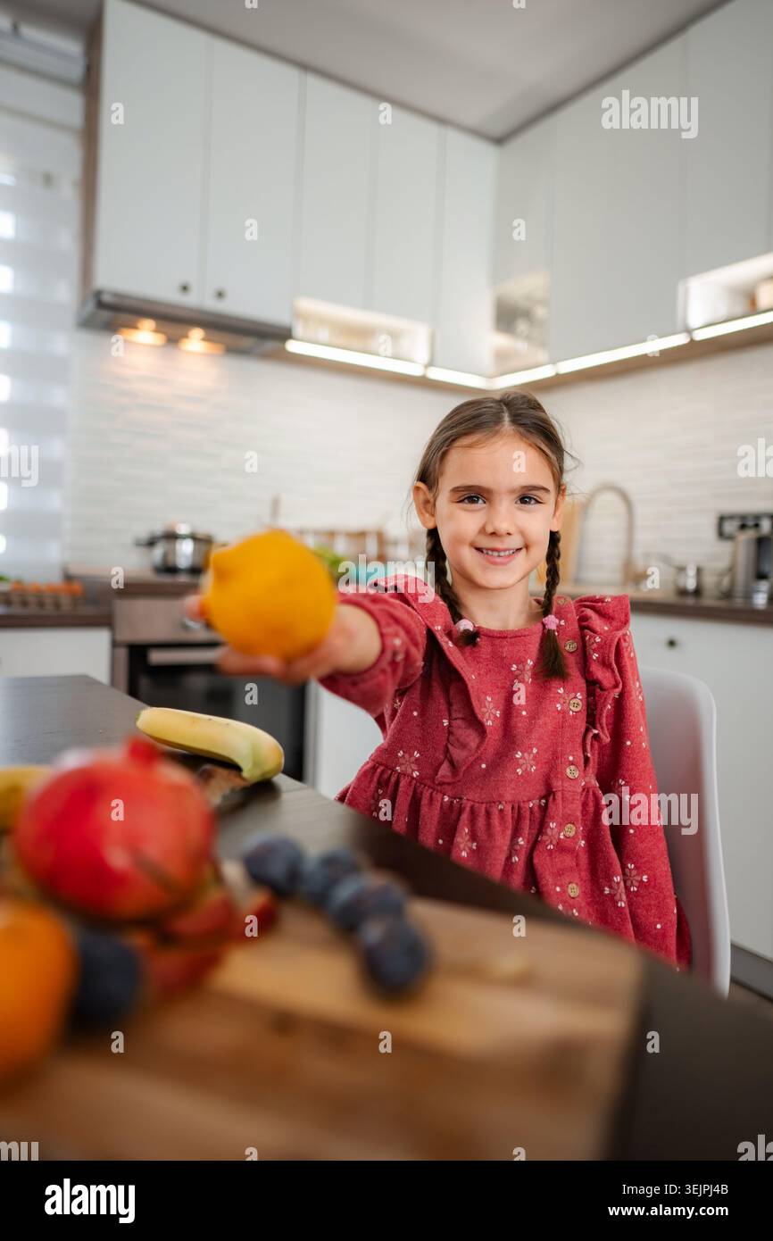 Ragazza che offre arancia fresca per uno spuntino sano nella cucina moderna Foto Stock