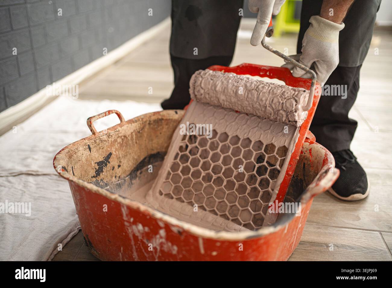 L'uomo immerge un rullo per pittura per rimuovere la vernice in eccesso dal tergivetro Foto Stock
