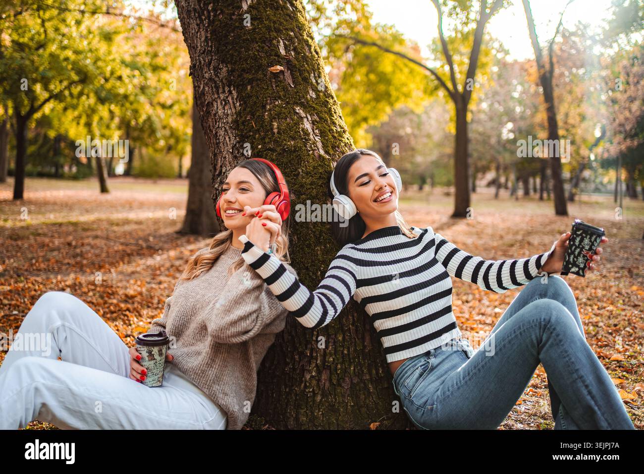Ragazze che amano le vibrazioni autunnali, le risate e la musica sotto gli alberi nel parco Foto Stock