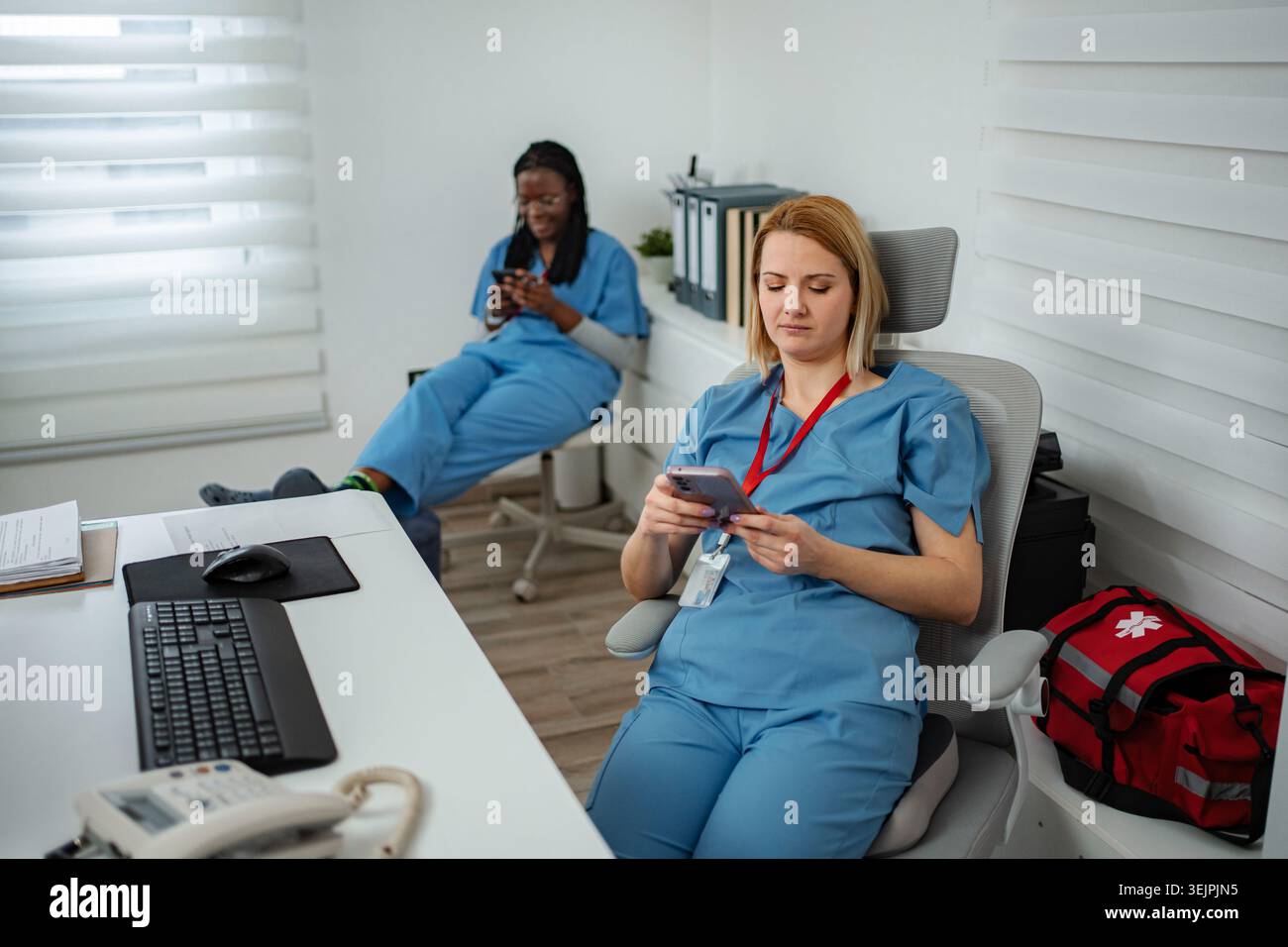 Infermieri in pausa che inviano messaggi di testo sui telefoni cellulari in clinica Foto Stock