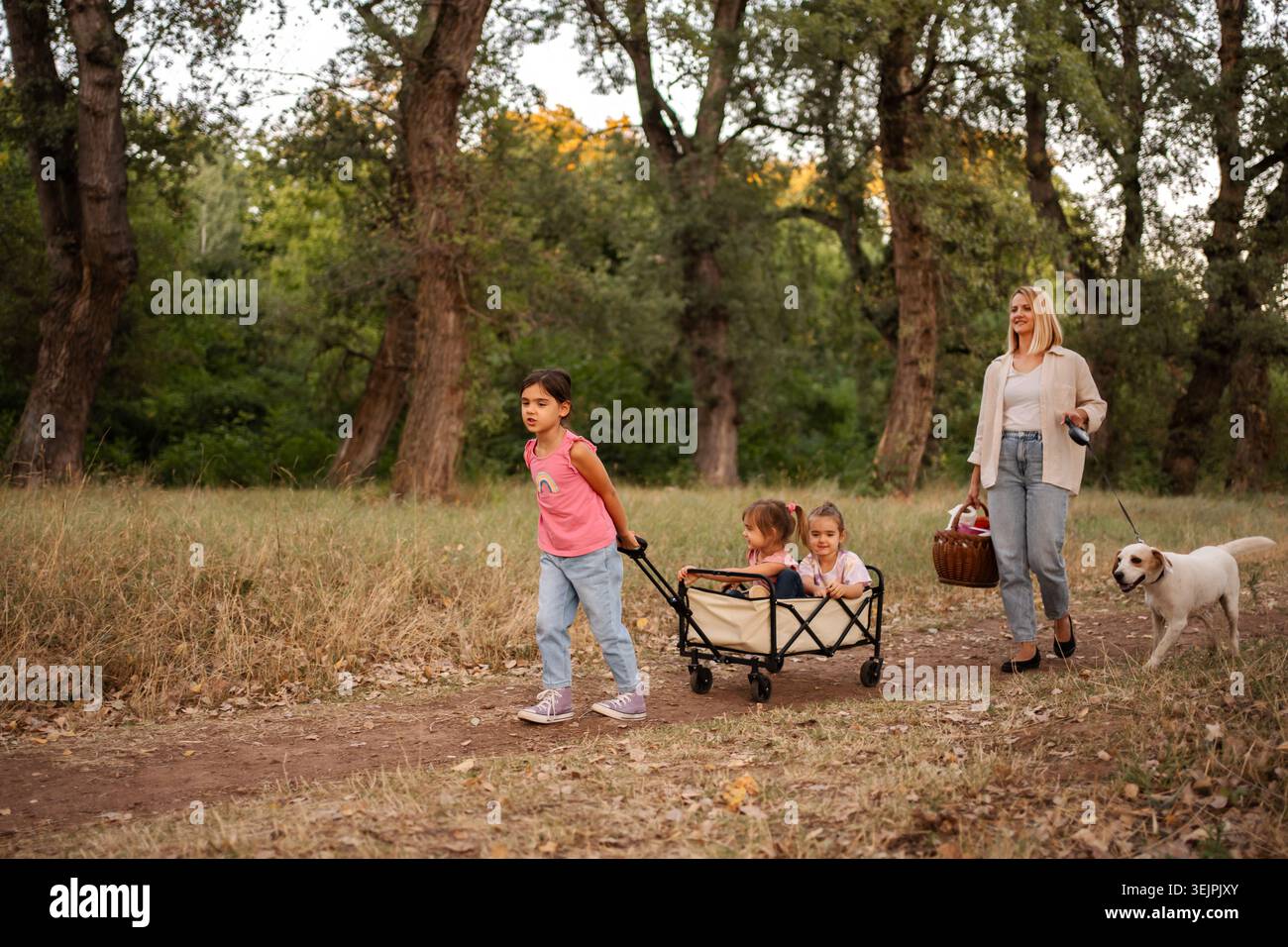 La famiglia si diverte a passeggiare nel bosco con il proprio cane e un carro Foto Stock