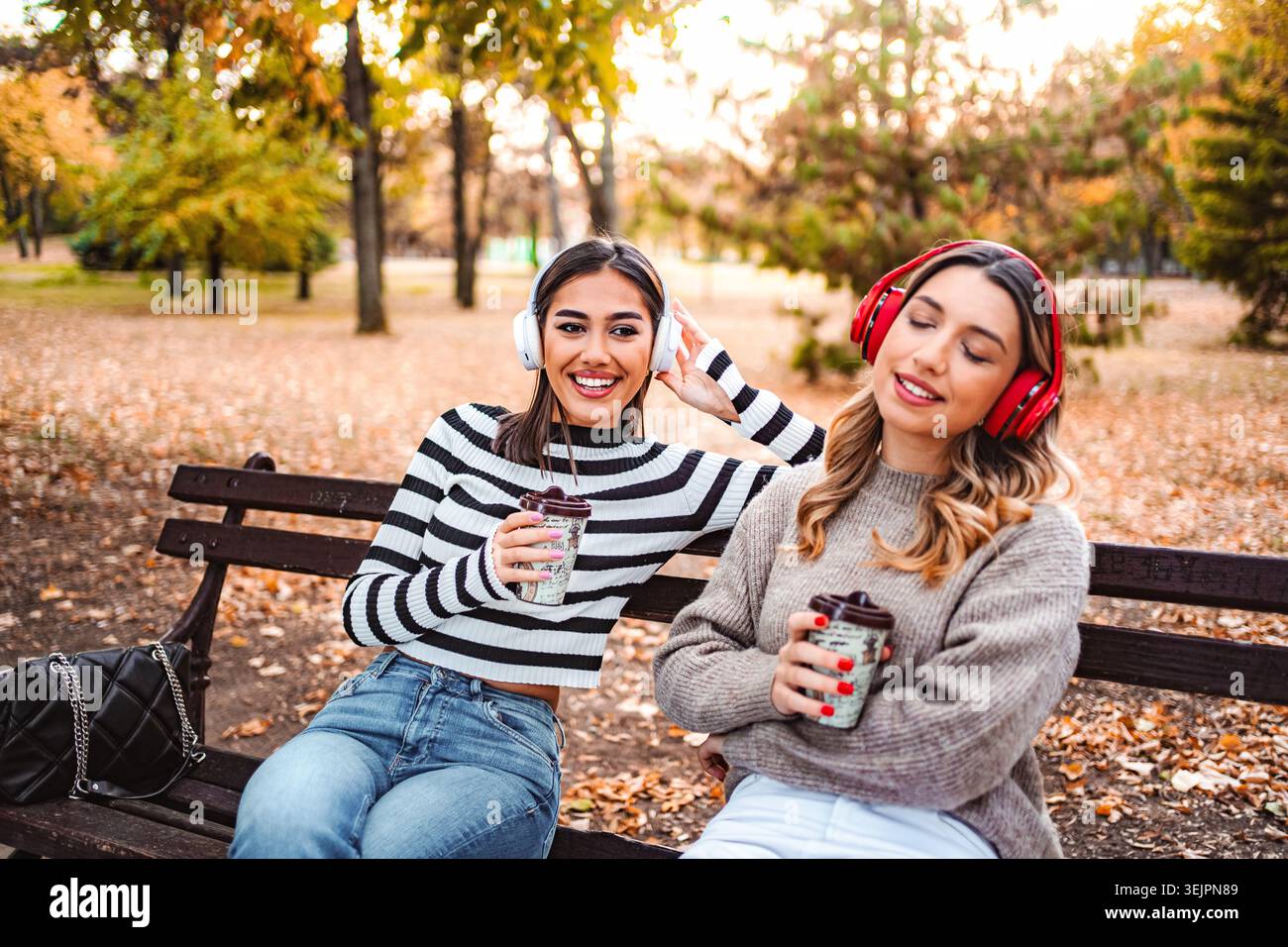 Due ragazze condividono musica e calore in un tranquillo parco autunnale Foto Stock