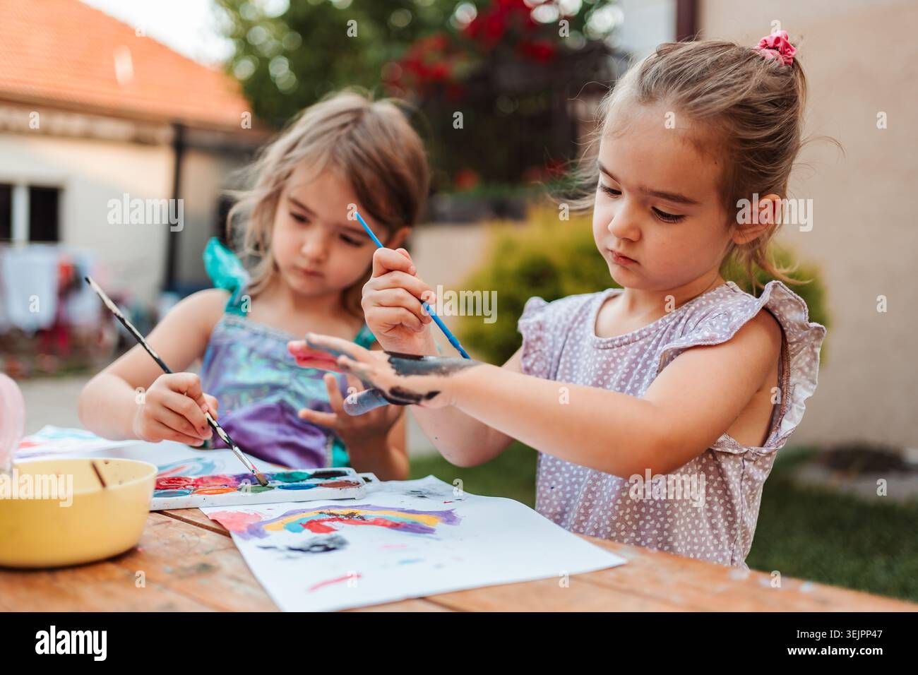 Due ragazze in età prescolare che dipingono con le dita e le spazzole nel cortile Foto Stock