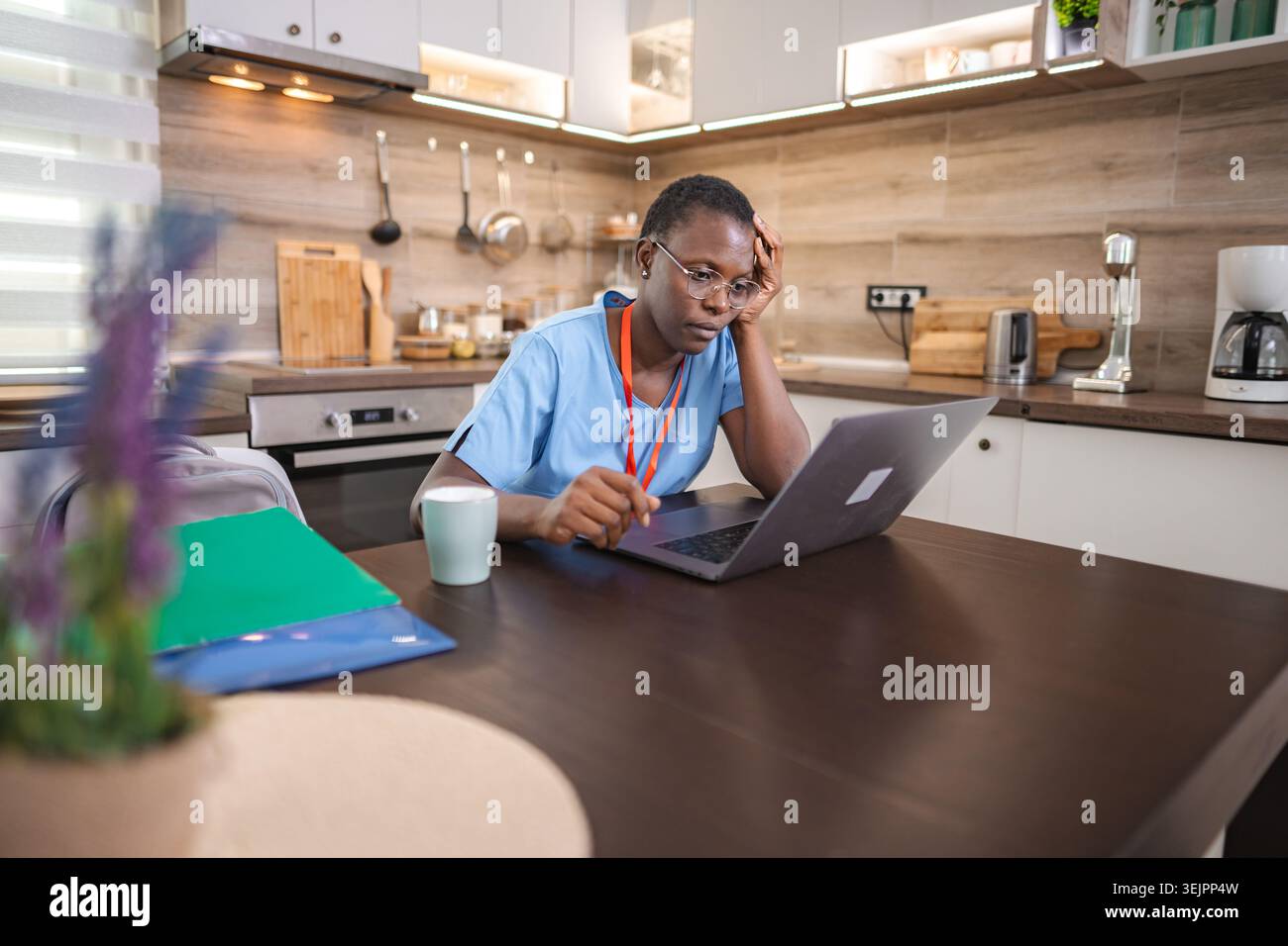 Infermiera stanca che lavora con un computer portatile in cucina dopo il turno di lavoro Foto Stock