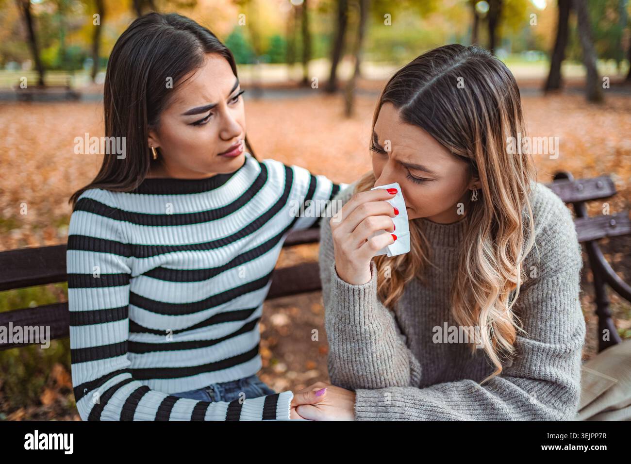 Due ragazze condividono un momento di cuore in un parco autunnale pieno di foglie cadute Foto Stock