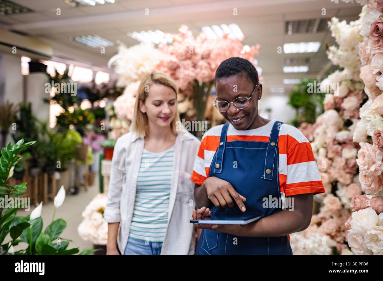 Fiorista che mostra le composizioni di fiori su un tablet a un cliente in un negozio di fiori Foto Stock