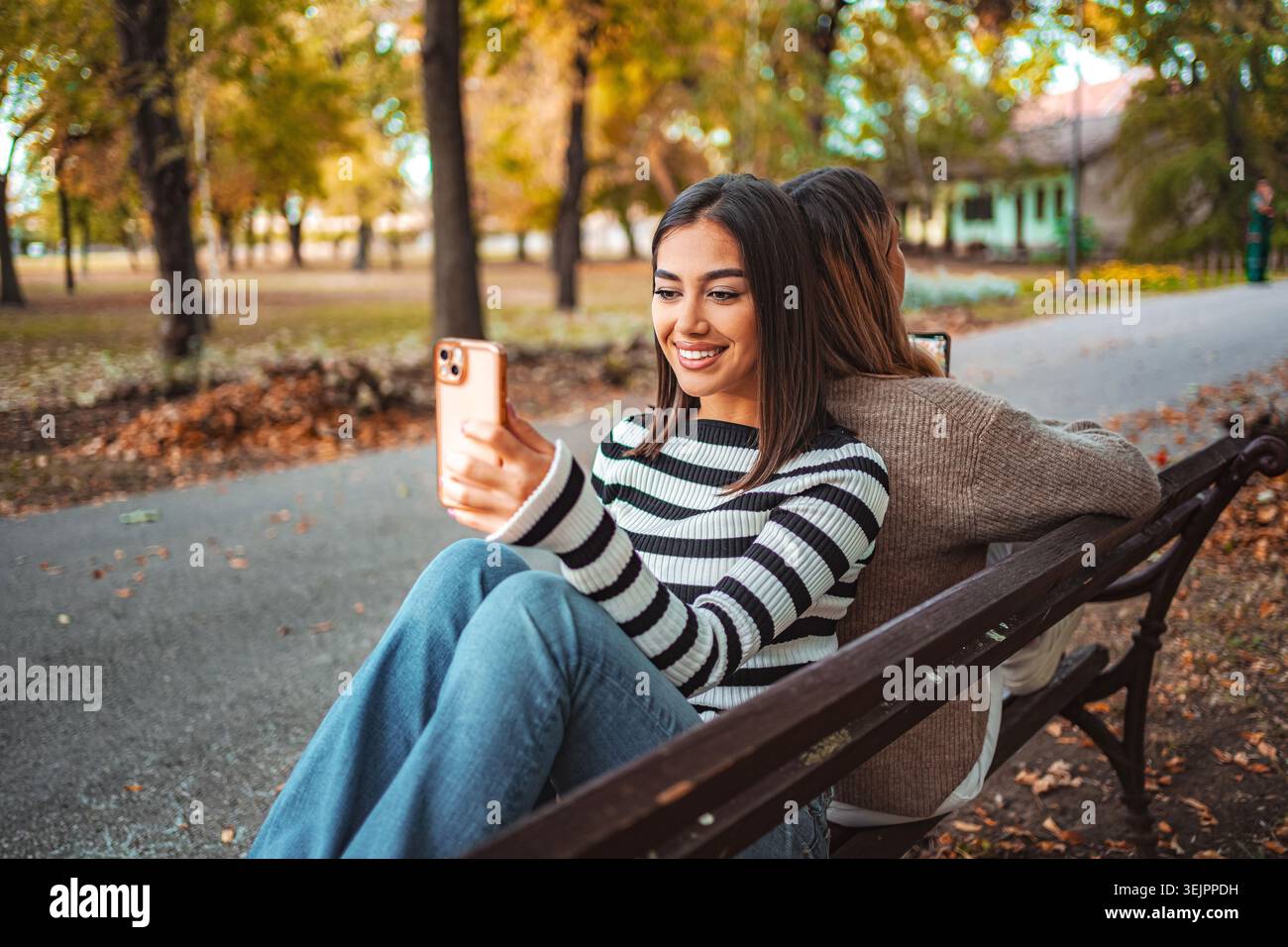 Due bambine si godono una soleggiata giornata autunnale nel parco mentre fanno selfie insieme Foto Stock