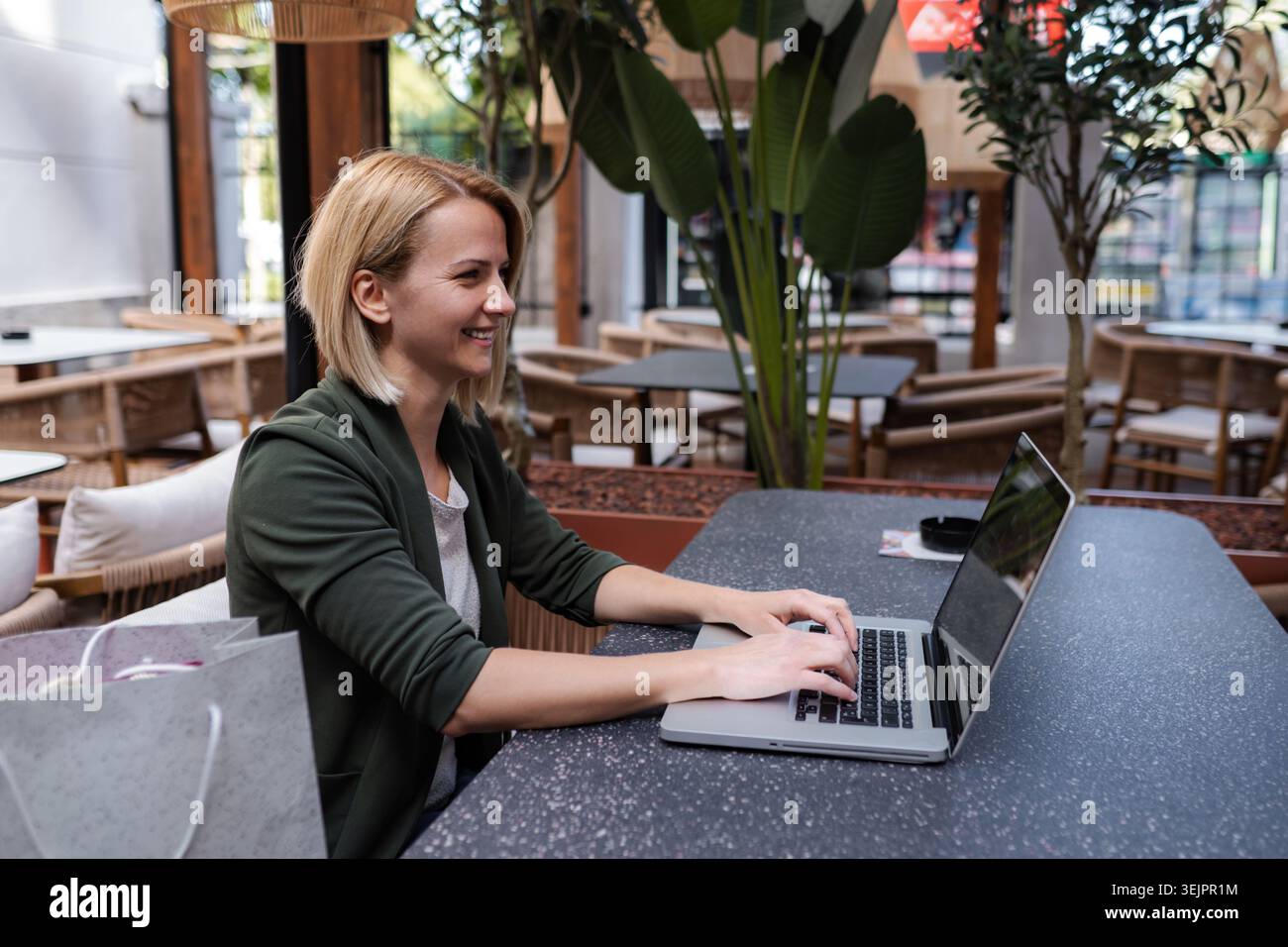 Donna che lavora con un laptop e sorride in un bar Foto Stock